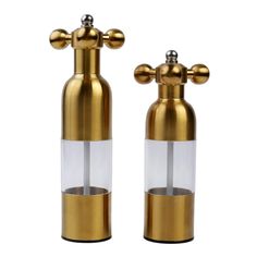 two brass and clear glass pepper shakers with metal caps on each side, one is holding an empty bottle