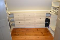 an empty closet with white cabinets and drawers on the wall, next to a wooden floor