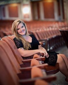 a woman is sitting in an empty auditorium with her legs crossed and smiling at the camera