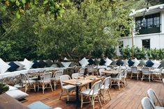 an outdoor seating area with tables and chairs on the wooden floor, surrounded by greenery