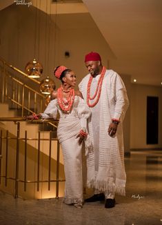 a man and woman standing next to each other in front of a stair case with gold railing