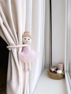 a little ballerina doll hanging from the side of a window sill in front of a curtain