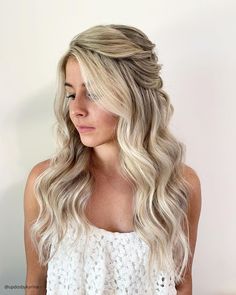 a blonde woman with long wavy hair wearing a white top and looking off to the side