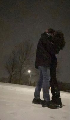 two people standing in the snow at night with their arms around each other and kissing