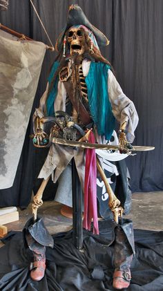 a skeleton sitting on top of a table next to a black cloth covered floor and holding two swords