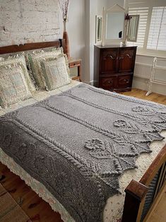 a bed with a gray blanket on top of it in a bedroom next to a dresser