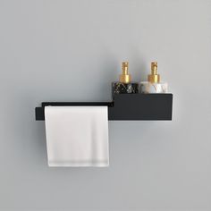 two soap dispensers and a towel hanging on a black shelf against a gray wall