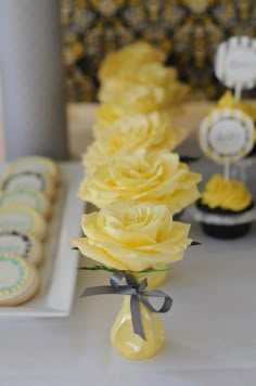 a table with cookies and cupcakes on it that have yellow roses in them