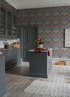 a kitchen with grey cabinets and floral wallpaper on the walls, along with wooden flooring