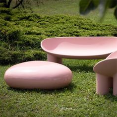 two pink benches and a stool in the grass near some bushes, one is shaped like a flowerpot