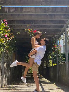 a man holding a woman on his back in front of a covered area with flowers