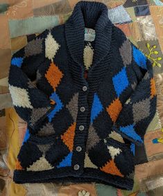 a knitted cardigan sitting on top of a patchwork quilted table cloth