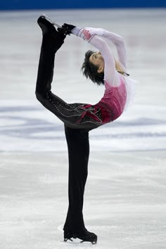 a female figure skating on the ice in a pink and black outfit with her arms extended