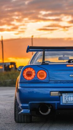 the back end of a blue sports car with its lights turned on at sunset or sunrise