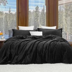 a black comforter set with white pillows in front of a window and trees outside