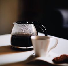 a coffee pot sitting on top of a table next to a cup