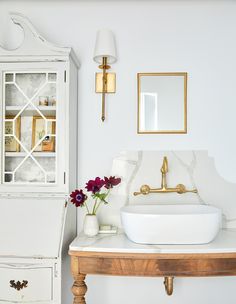 a white sink sitting on top of a wooden table next to a vase with flowers