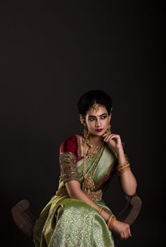 a woman in a green and gold sari sitting on a chair with her hand under her chin