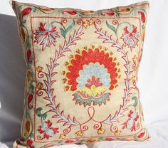 an embroidered pillow on a white background with red, yellow and blue flowers in the center