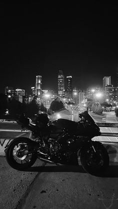 a black and white photo of a motorcycle parked in front of a cityscape