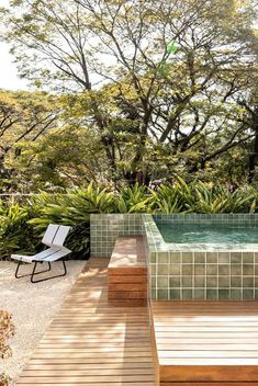 a wooden deck next to a pool surrounded by lush green trees and bushes, with a lounge chair in the foreground