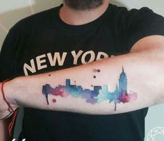 a man's arm with a watercolor skyline tattoo on it