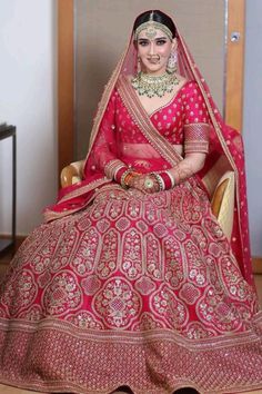 a woman sitting in a chair wearing a red and gold bridal gown