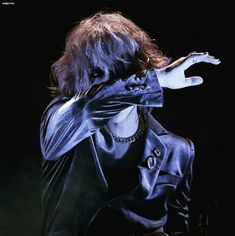 a man with long hair covering his face while standing in front of a black background