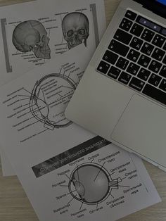 an open laptop computer sitting on top of a wooden table next to papers with diagrams