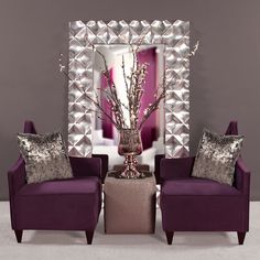 two purple chairs sitting next to each other in front of a mirror and vase with flowers