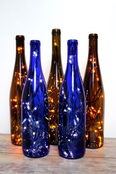 three blue glass bottles sitting next to each other on top of a wooden table with lights in them