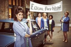 a woman standing next to a car in front of a group of women holding a sign