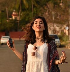 a woman standing in the middle of a street holding two cell phones