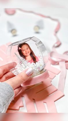 a person holding a snow globe with a photo in it and pink ribbon around the edges