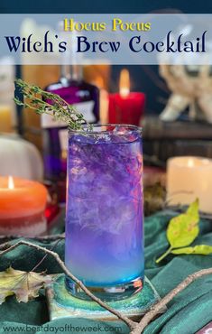 a glass filled with purple and blue liquid sitting on top of a table next to candles