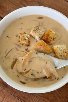 a white bowl filled with soup and croutons on top of a wooden table