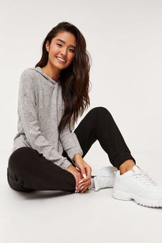 a woman sitting on the ground wearing black pants and a grey sweater with white sneakers