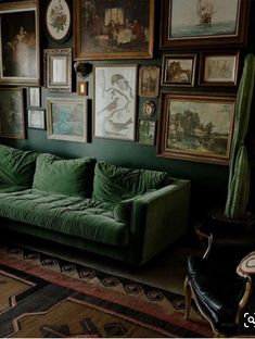 a green couch sitting in front of a wall covered with pictures and paintings on it