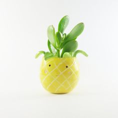 a yellow pineapple shaped planter with green leaves in the shape of a smiley face