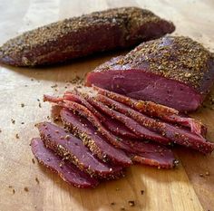 sliced meat sitting on top of a wooden cutting board next to seasoning sprinkles