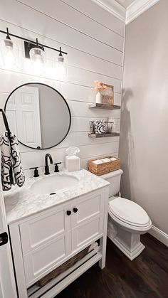 a white toilet sitting next to a sink in a bathroom under a mirror and lights