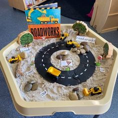 there is a sand tray with construction vehicles and books in it on the floor next to a bookcase