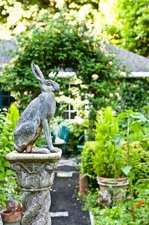 a statue of a rabbit sitting on top of a stone pillar in the middle of a garden