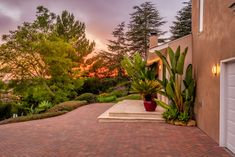 a brick driveway leading to a house with trees in the back ground and bushes on either side