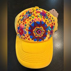 a yellow hat with colorful designs on it sitting on a black table next to a tag