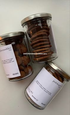 three glass jars filled with cookies on top of a white table next to each other