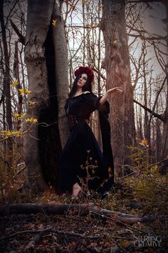 a woman in a black dress standing next to a tree and holding her hand out