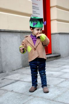 a little boy wearing a green hat and holding an apple in his hand while standing on the sidewalk