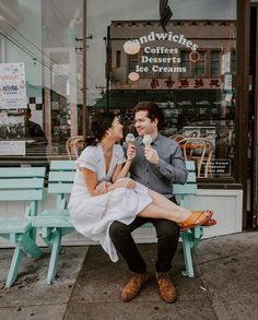 a man and woman sitting on a blue bench in front of a coffee shop eating ice cream