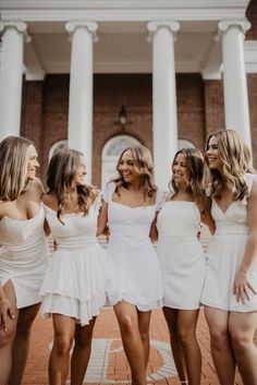 four beautiful women in white dresses posing for a photo together on the steps of a building